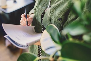 Frau steht im Büro und schreibt in ihr Notizbuch Frau steht im Büro und schreibt in ihr Notizbuch