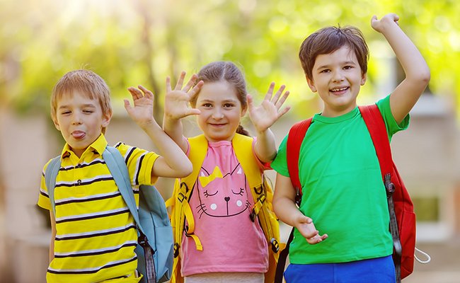 Gruppe von Kindern steht mit Rucksäcken in der Nähe der Schule