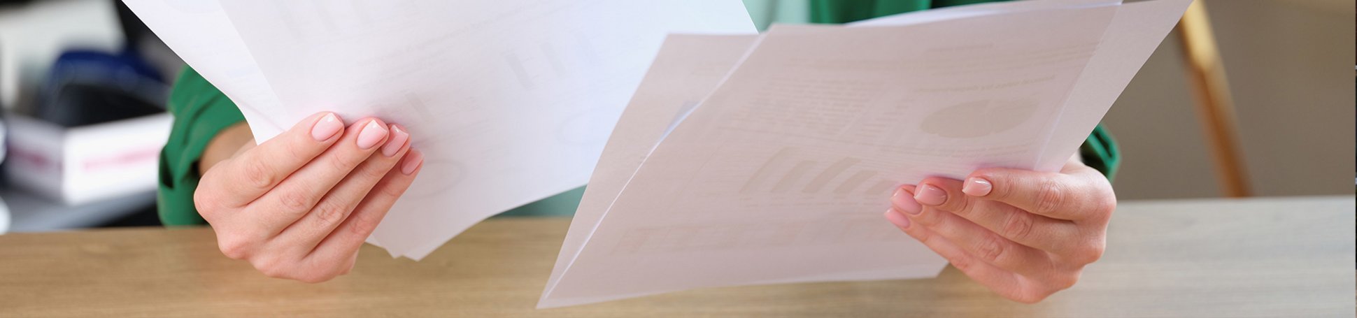 Frau sitzt am Schreibtisch und hält viele Dokumente in den Händen