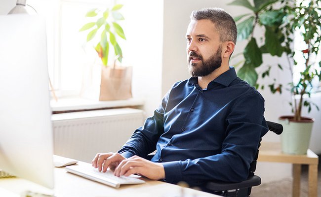 Mann im Rollstuhl arbeitet am Schreibtisch
