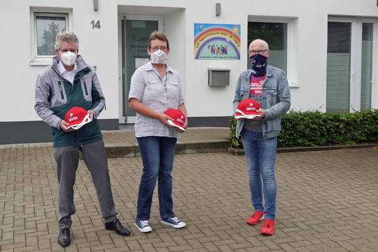 Dekra-Niederlassungsleiter Carsten Debler (links) überreichte gemeinsam mit Bürgermeister Fred Toplak (rechts) signalrote Sicherheitskappen an Simone Wallbaum (Mitte), Leiterin des katholischen Kindergartens St. Ludgerus.