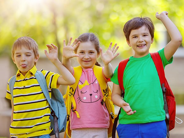 Gruppe von Kindern steht mit Rucksäcken in der Nähe der Schule
