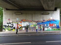 Foto: vier Personen stehen unter einer Autobahnbrücke vor einem bunten Graffitti