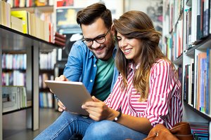 Ein junges Paar schaut in der Stadtbibliothek auf ein Tablet Ein junges Paar schaut in der Stadtbibliothek auf ein Tablet