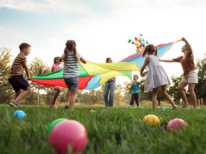 Kinder spielen mit einem Regenbogen-Spielplatzfallschirm 